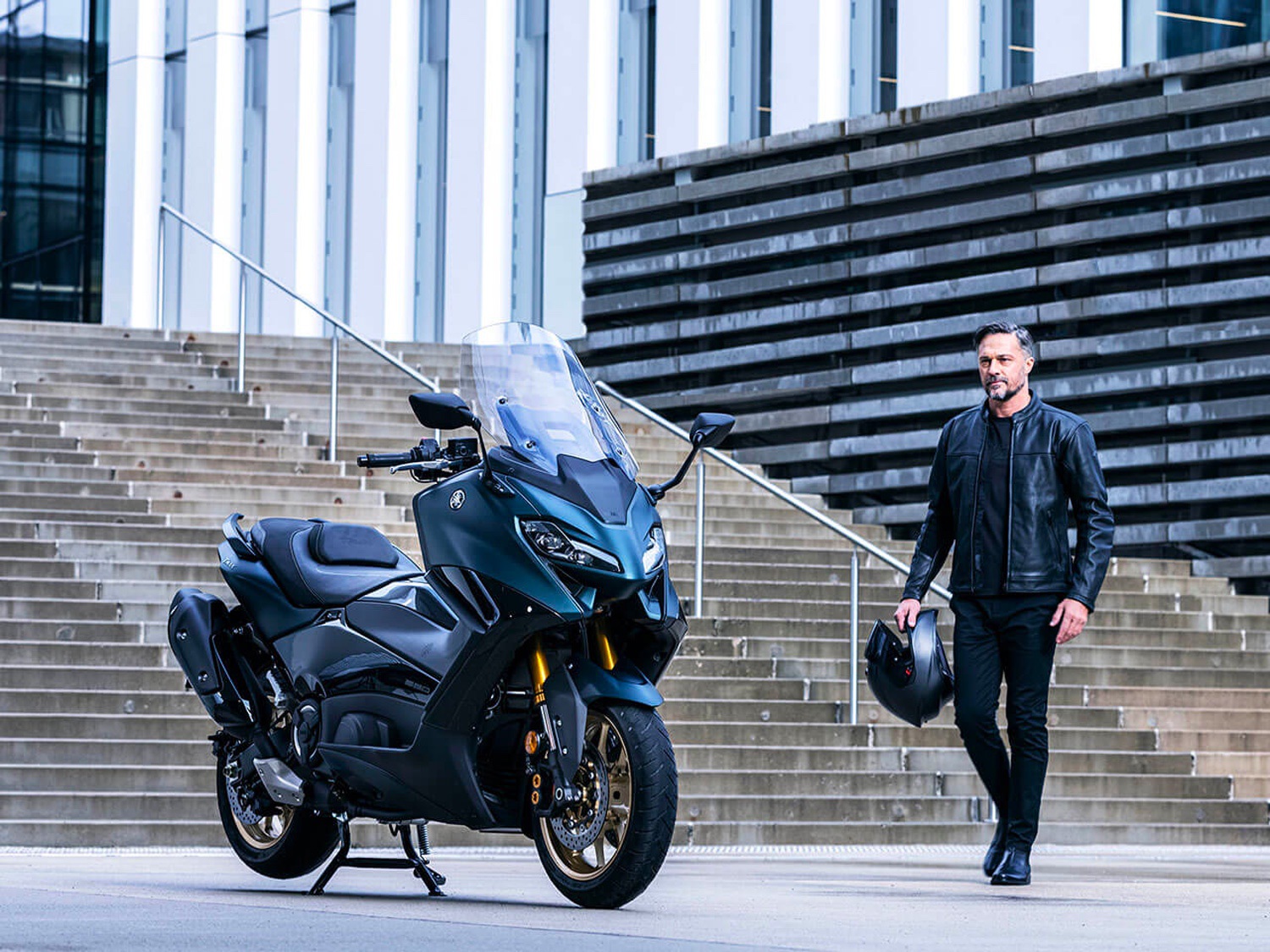 A man approaches a 2022 Yamaha TMAX Tech MAX Scooter outside in the city